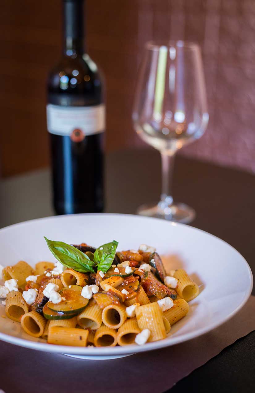 A plate of pasta and a bottle of wine on a table.